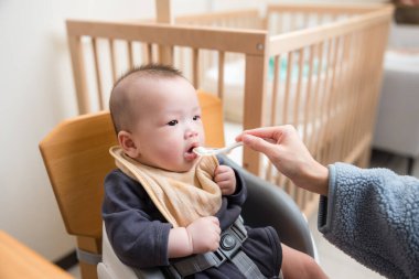 Anne evde kaşıkla bebeğini besliyor.