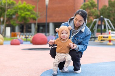 Anne, dışarıda çocuk parkında bebeğe yardım ediyor.