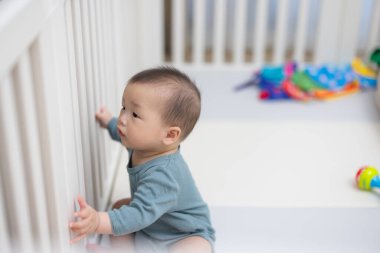 Bebek oyun parkında otururken beyaz beşiğe dokunuyor