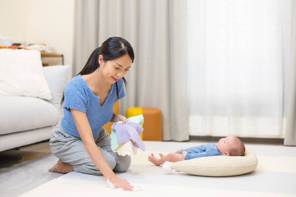 Mum tidying playpen with baby at home in morning
