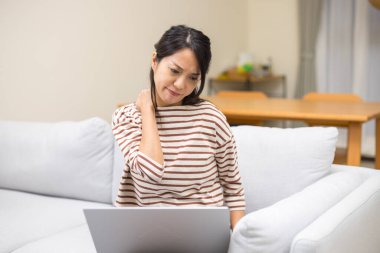 İçerde dizüstü bilgisayar kullanan bir kadın omuz ağrısı çekiyor.