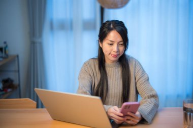 Gece evde dizüstü bilgisayar ve telefon kullanan bir kadın.