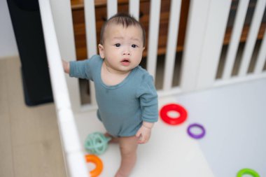 Bebek beşikte beyaz korkulukları tutuyor.