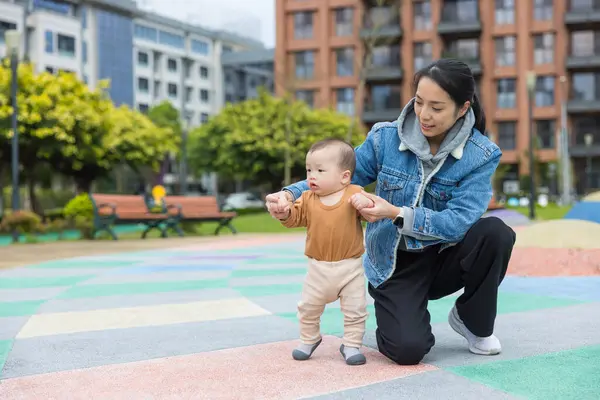 Yürümeye yeni başlamış bir çocuk, annesiyle parkta yürüyor.