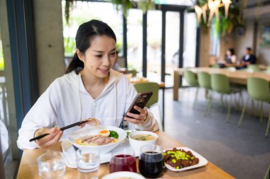 Restoran masasında yemek yerken telefon kullanan bir kadın.
