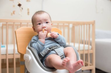 Bebek sandalyesinde oturup yemek yiyor.