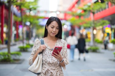 Sokakta yürüyen bir kadın telefona bakıyor.