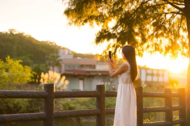 Altın saat boyunca telefon kamerası kullanan genç bir kadın.