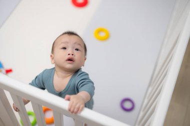 Meraklı bebek beyaz beşikte dikilip yukarı bakıyor