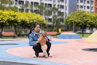 Anne oğluna parkta yürümeyi öğretiyor.