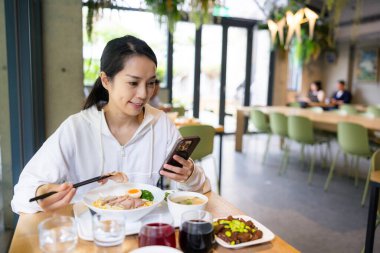 Restoran masasında yemek yerken telefona bakan bir kadın.