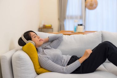 Kanepeye uzanmış, kulaklıkla dinlenen bir kadın.