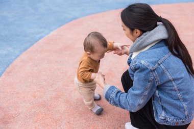 Anne, bebeğinin parkta yürümesine yardım ediyor.