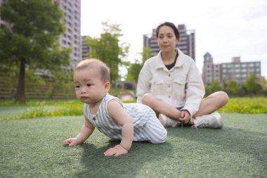 Annesiyle parkta çimenlerde sürünen bir bebek.