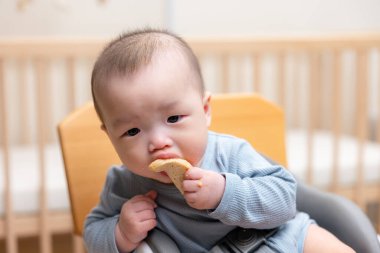 Asyalı bebek sandalyede oturmuş pirinç krakeri yiyor.