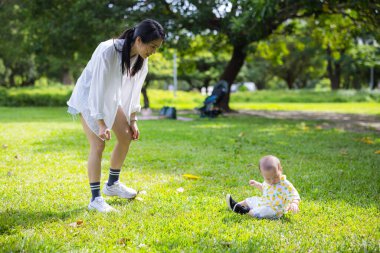 Bebek parkta annesiyle çimlere oturur.