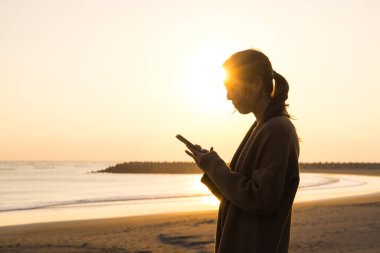 Kadın deniz kenarında cep telefonu silueti kullanıyor