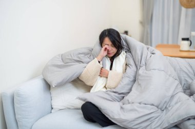 Kalın bir battaniyeyle örtülmüş bir kadın kendini hasta hissediyor.