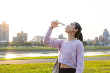 Park yerinde duran bir kadın taze su içiyor.