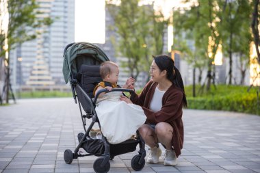 Bakıcı anne bebeği parkta yürüyüşe çıkarıyor.