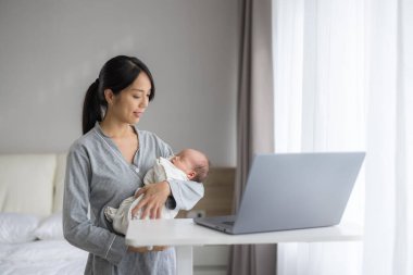 Anne dizüstü bilgisayar kullanırken yeni doğmuş bebeğe bakıyor.