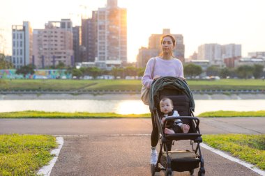 Annem bebekle birlikte yeşil parka doğru bebek arabasını itiyor.