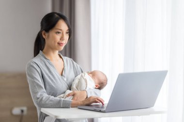 Anne dizüstü bilgisayarda çalışırken bebeğe bakar.
