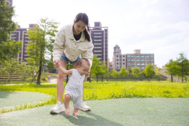 Yeni yürümeye başlayan çocuğun ilk adımlarını atmasına yardım eden kadın.