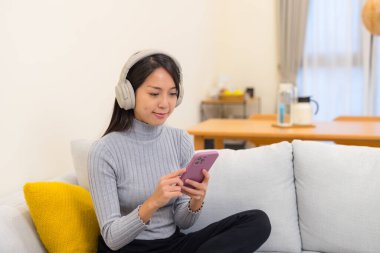 Kulaklıkla cep telefonu ekranına bakan bir kadın.