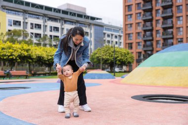 Anne oğlunu kucağına al ve şehir parkında ilk yürüyüşe çık.