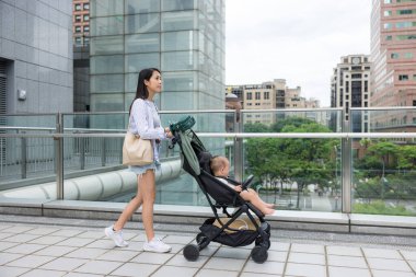 Genç anne, bebek arabasını şehir sokaklarında itiyor.