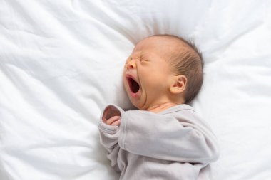 Yeni doğmuş bebek yumuşak yatakta huzur içinde esniyor.