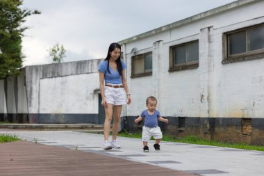 Anne, bebeğin eski binanın yakınındaki patikada yürümesini izliyor.