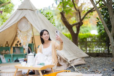 Kadın kampa gider çadırın dışında oturur ve selfie çeker.
