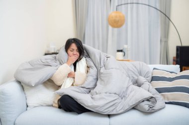 Sıcak battaniyeye sarılmış hasta kadın hapşırıyor.