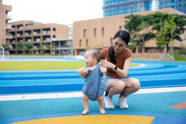 Anne, bebeğe şehir parkında ilk adımları atmasında yardım ediyor.