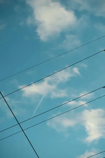 stock image A serene sky crossed by power lines and a high-flying jet's contrail, blending technology with nature's vastness.