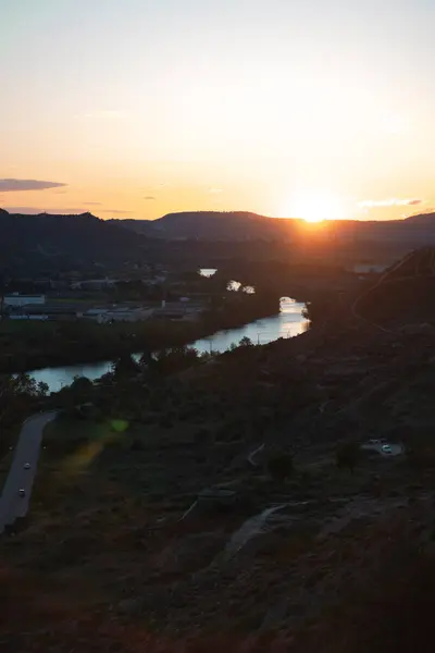 川の渓谷を眺め 水面を反射する黄金の輝きを投げかけ 周囲の丘と遠くの都市景観の静けさを強調した美しい夕日 — ストック写真
