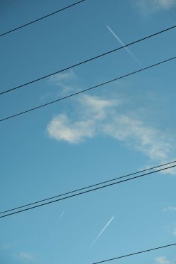 A serene sky crossed by power lines and a high-flying jet's contrail, blending technology with nature's vastness. clipart
