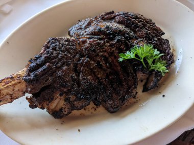 Tomahawk bifteğinde kavrulmuş kemik ve beyaz tabakta maydanoz..