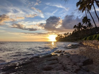 Watching the sun dip below the horizon: a mesmerizing sunset over the rugged coastline of Diamond Head Beach in Oahu, Hawaii.