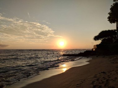 Serene serenade: The sun sets over Waikiki waters as the rhythmic waves roll into shore at Makalei Beach Park on Oahu, Hawaii.
