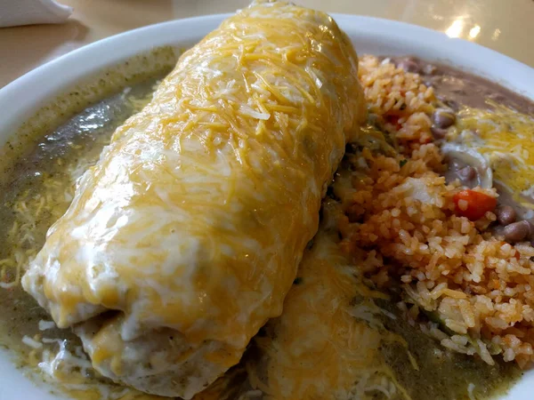 Wet Burrito with rice and beans on Plate on top table with knife and fork.