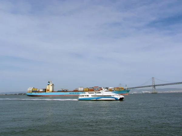 サンフランシスコ 2009年3月25日 巨大な船の雄大な存在に囲まれたサンフランシスコの象徴的なベイブリッジと 前景を航海するフェリーボート 忘れられない瞬間 — ストック写真