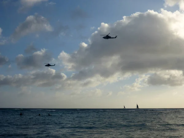 ワイキキ 4月11 2019 夕暮れ時のワイキキの水 海を航行するボート 空を飛ぶ2つの軍用ヘリコプター 海水浴やサーフィンを楽しむ人もいれば ビーチでリラックスする人もいます これはオアフ島の典型的なシーンです — ストック写真