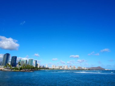 Hawaii, Oahu 'nun güney kıyısında popüler bir sörf merkezi olan Kewalo Basin Point' te dalgaları yakalayan sörfçüler. Fotoğraf ayrıca, Hawaii 'nin başkenti ve en büyük şehri olan Honolulu kıyılarını çevreleyen apartman ve binaları da gösteriyor.. 