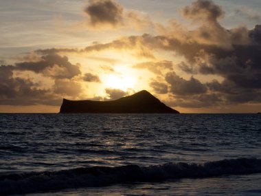 Tavşan Adası ve Waimanalo Körfezi üzerinde gün doğumunun nefes kesici bir fotoğrafı, Hawaii 'nin Oahu adasındaki en manzaralı ve tarihi yerlerden ikisi. Fotoğraf, turuncu güneşin bulutların arkasından yükselişini ve suyun üzerinde sıcak bir parıltı oluşturuşunu gösteriyor.