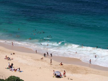 Oahu - 31 Mart 2013: Havai 'deki Makapuu Sahili manzaralı, yüksek görüş açısına sahip bir yer. Kumsal kumlu ve üzerinde birkaç şemsiye ve insanlar var. Okyanus güzel mavi-yeşil bir renktir ve kıyıya vuran küçük dalgaları vardır..