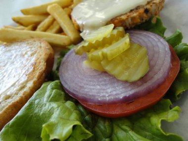 Lezzetli bir açık sebzeli burger, yanında da patates kızartması. Hamburger, üzerinde bir dilim domates, bir dilim kırmızı soğan ve bir turşu olan bir marul yatağında. Sebze ve tahıldan yapılmış hamburger köftesi. Kızartmalar altın gibi.