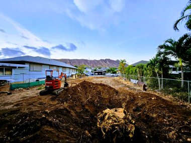 Honolulu - 29 Eylül 2023: İkamet yerindeki boş bir arsa ağır makinelerle inşaata hazırlanıyor. Fotoğraf kırmızı Hitachi kazıcısını gösteriyor. Etrafı tel örgülerle çevrili. Fotoğrafta ayrıca...